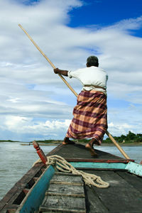 Rear view of man fishing at sea shore against sky