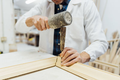 Hands of craftsman using work tool to make frame in workshop