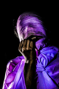 Portrait of person covering face against black background