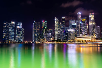 Illuminated buildings by river against sky in city at night