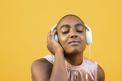Woman listening music against yellow background