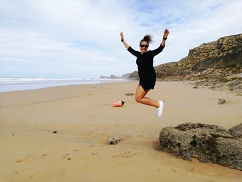 Full length portrait of woman jumping at beach against sky