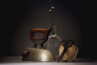 Iron with scissors and thread by glass bottle against black background