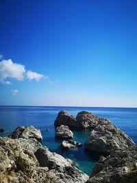 Rocks by sea against blue sky