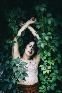 Close-up portrait of young woman with arms raised standing amidst plants