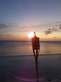 Electric lamp on beach against sky during sunset