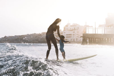 Pulled back view of mother and son surfing a small wave at sea