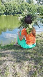 Rear view of woman sitting on grass by lake