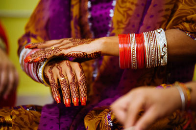 Midsection of woman with henna tattoo wearing red bangles