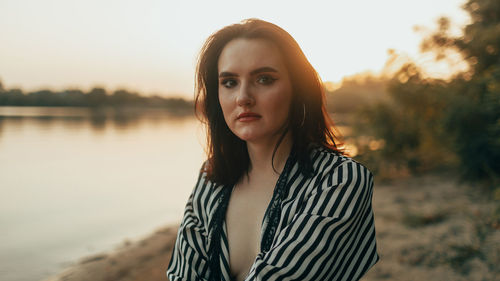 Portrait of young woman standing against lake