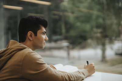 Thoughtful young male student studying at table in university