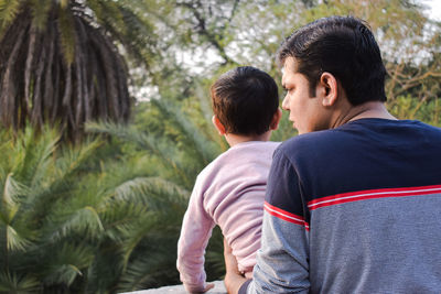 Rear view of friends with arms raised against trees