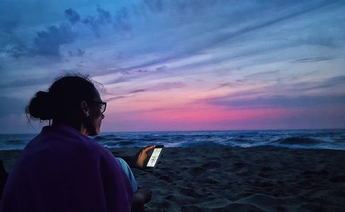 Rear view of man on beach against sky during sunset