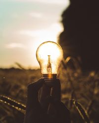 Close-up of hand holding light bulb against sky