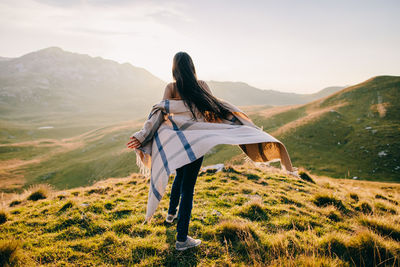 Rear view of woman with arms outstretched on mountain against sky during sunset