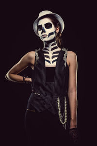 Portrait of woman with skull face paint while standing against black background