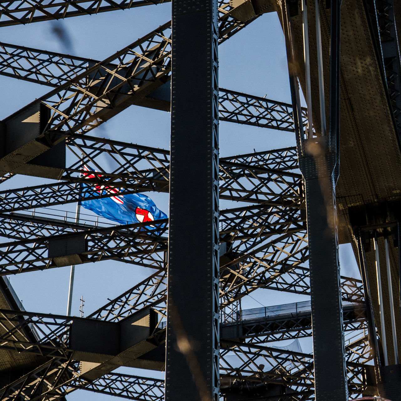 architecture, built structure, metal, low angle view, day, outdoors, nature, no people, sky, arts culture and entertainment, connection, bridge, bridge - man made structure, blue, flag, travel destinations, city, grid