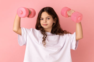 Portrait of young woman lifting dumbbells against yellow background