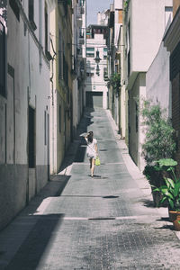 Rear view of woman walking on footpath amidst buildings