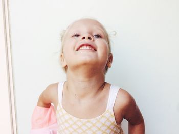 Close-up portrait of cheerful girl standing against white wall