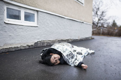 Unconscious woman in medical shock lying under emergency blanket in street