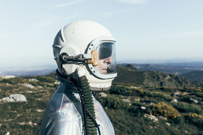 Side view male astronaut in spacesuit and helmet standing on grass and stones in highlands