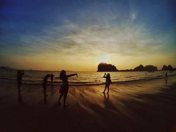 Silhouette people at beach against sky during sunset