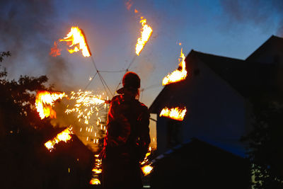 Rear view of fire dancer by house against sky during sunset