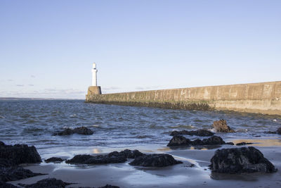 Lighthouse by sea against clear sky during winter