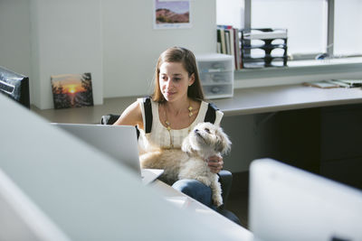 Businesswoman with dog using laptop computer at desk in office