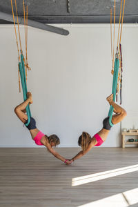 Women holding hands hanging from aerial silk in health club