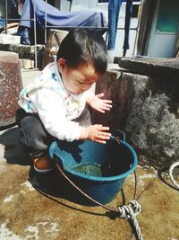 Full length of cute baby boy crouching by bucket during sunny day