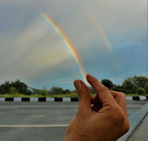 Close-up of hand holding rainbow over road against sky