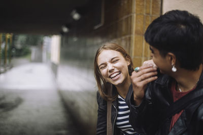 Cheerful girl laughing with teenage male friend near wall