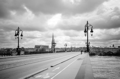 Bridge over river by church against cloudy sky in city