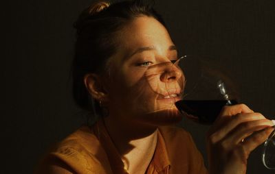 Close-up of woman drinking wine against wall