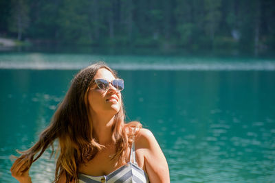 Young woman wearing sunglasses against lake and trees