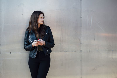 Beautiful young woman using phone against metallic wall