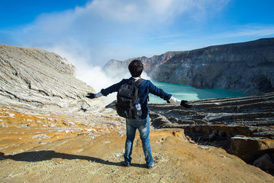 Rear view of man standing on rock against sky