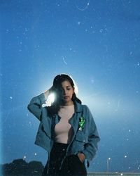 Young woman with hand in hair standing against blue sky during snowfall