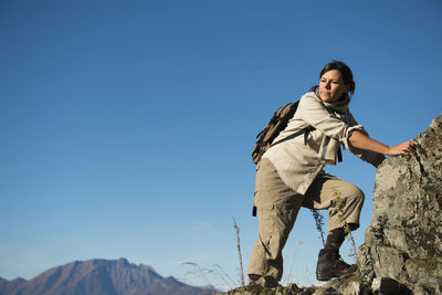 Female hiker hiking on rock against blue sky