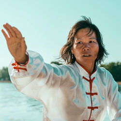 Woman practicing martial arts at lake against sky
