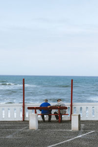 Rear view of man sitting on chair at beach against sky