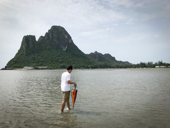 Man with umbrella walking on beach against mountain