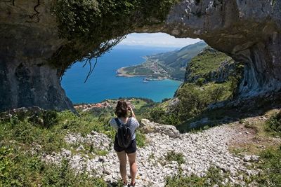 A young woman takes photos through a natural arch on top of the mountain