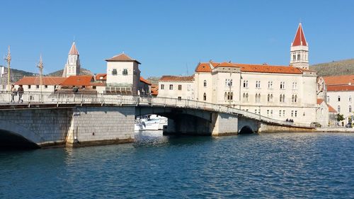 Bridge over river in town against clear blue sky