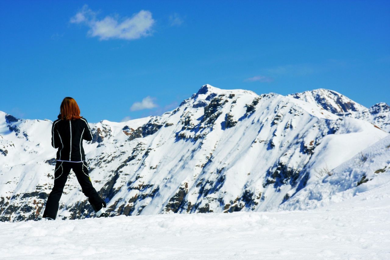 REAR VIEW OF WOMAN STANDING ON SNOW COVERED MOUNTAINS