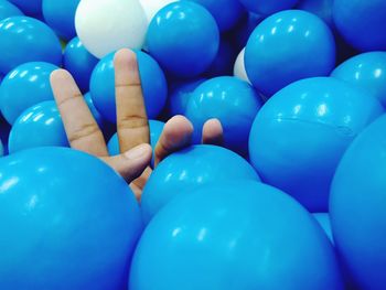 Cropped hand gesturing peace sign amidst blue balls