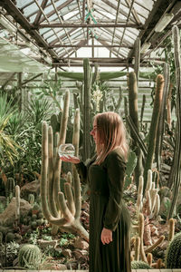 Side view of woman holding container while standing in greenhouse