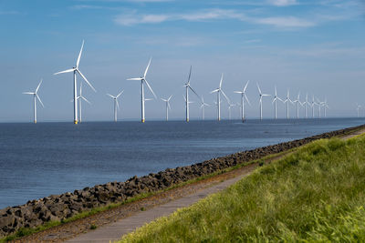 Windmills by sea against sky